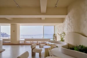 Coastal living room with modern design, white walls, beige furniture, and a large window overlooking the ocean