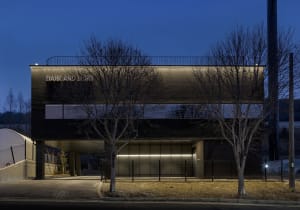 A modern building with a black facade and a large window, surrounded by trees and greenery