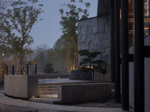 A modern house at night with a large stone building and black doorway, surrounded by trees and artificial lighting