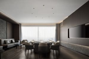 A modern dining area with a large wooden table, multiple chairs, and various table settings, surrounded by white walls and wooden floors