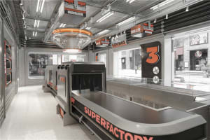 Industrial workspace with a large counter and conveyor belt system, featuring three clocks on the wall and a functional atmosphere