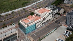 A modern building with a red roof and a staircase made of concrete, set against a white background