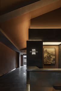 A warm and inviting hotel lobby with a large stone wall, a countertop, two chairs, and a painting on the wall