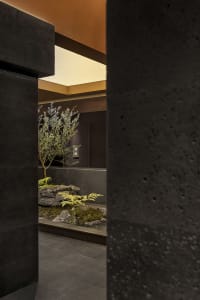 A serene indoor space with a small tree in a rock garden surrounded by concrete walls and two large rocks, creating a peaceful atmosphere