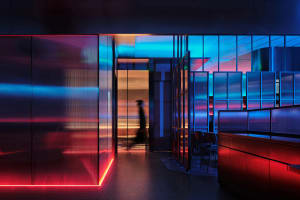 A modern office hallway with red accents, chairs, and a woman walking down the hall at night