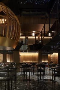 Dimly lit modern restaurant interior with multiple tables and chairs, wine glasses, and a sophisticated atmosphere