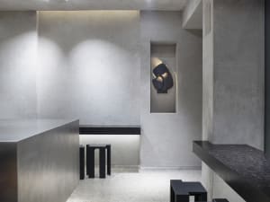 Empty minimalist room with a concrete wall, black countertop, and a dining table, featuring two chairs and a functional atmosphere