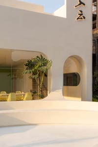 A modern living area with a large concrete wall, chairs, and potted plants, featuring a minimalist aesthetic with clean lines and simplicity