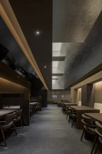 Modern restaurant interior with concrete walls, overhead lighting, and a large dining area with tables and benches