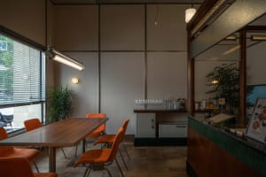 Warm and inviting restaurant interior with a wooden table, orange chairs, and wine glasses, set against a neutral background