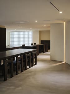 A spacious restaurant with a long dining table, wooden chairs, and a clean atmosphere, ready for customers