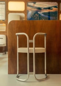 A modern kitchen with a wooden countertop, metal chairs, and framed artwork, set in a well-lit space