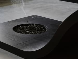 A modern indoor space with a black table and fire pit surrounded by rocks, with a small flame and a cozy atmosphere