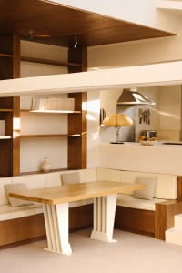 A cozy living space with a wooden dining table, surrounded by chairs, books, and decorative bowls, set in a warm and inviting atmosphere