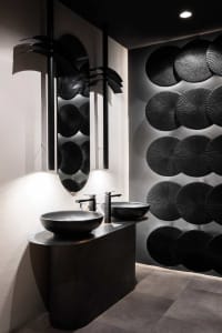 Bathroom with two sinks under a mirror, stone walls, and a large mirror above the sinks