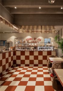 A restaurant interior with a checkered tile floor, dining tables, chairs, and counters displaying food items