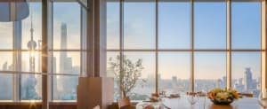 Modern dining area with chairs around a table, wine glasses, and a large window offering a city skyline view