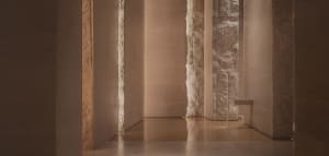 Grand hallway with stone walls, marble floors, and two large pillars, featuring a classical style and warm lighting