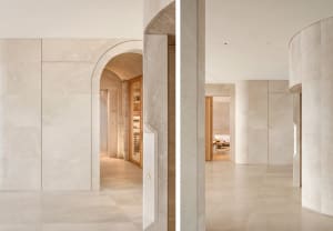 Open concept living area with marble walls, a large archway, and a dining table, with and without wine bottles on the countertop