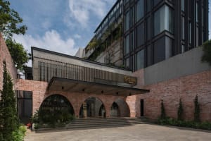 A modern building with a brick facade, featuring a large archway, balcony, and potted plants, with two benches and a welcoming atmosphere