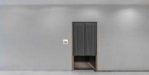 A minimalist hallway with a gray curtain-drawn doorway on a white wall, with no other visible features