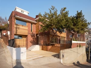 A charming house with a red brick exterior, surrounded by trees and a parked car, set against a natural background