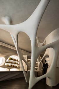 A modern bar area with a white sculpture, bottles, and a patron, set in a stylish and welcoming atmosphere