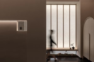 A person walks through a calm and serene interior space with two potted plants and a vase on a surface near the center