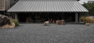 An outdoor area with two large rocks, chairs, and dining tables on a gravel ground, creating a casual and inviting atmosphere