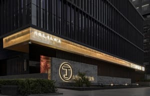 Modern office building with a black facade, lit windows, and a bench in front