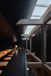 A modern black interior space with concrete walls, wooden floors, and various furniture pieces including chairs and dining tables