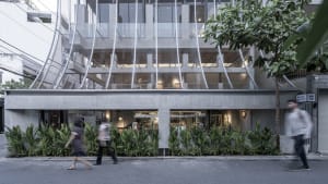 A bustling street scene with a modern building featuring a large glass wall, surrounded by people walking by