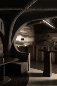 Industrial kitchen with stainless steel surfaces and a stone wall, featuring two sinks, a dining table, chairs, and a couch