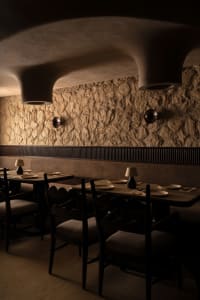 A cozy restaurant interior with a long dining table, wooden chairs, and lamps providing warm illumination