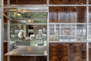 Industrial kitchen with two ovens, a sink, and three people in white uniforms preparing food in a professional and organized workspace