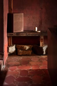 A rustic kitchen dining space with red walls, a tile floor, and a dining table with a chair, featuring two large rocks as design elements