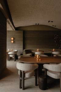 Modern restaurant interior with a large dining table, concrete walls, and lamps providing lighting