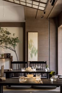 A warm and inviting dining area with a wooden table, chairs, bowls, cups, and vases, lit by natural sunlight through windows