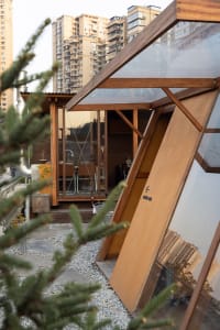 A modern house with a wooden structure and glass walls, featuring a large window and potted plants, with a clean and minimalistic design