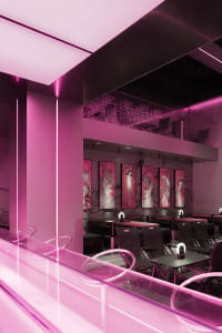 A modern restaurant interior with pink walls, multiple dining tables, and chairs, creating a warm and inviting atmosphere