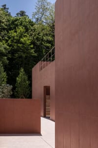 A red building with a staircase leading to a doorway, featuring two sets of stairs made of concrete, in a scene suggesting earthy tones and materials