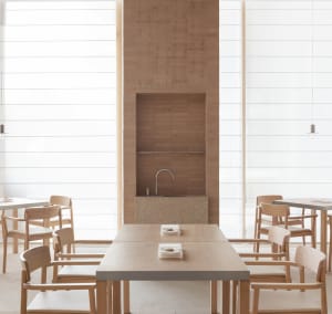 A well-lit restaurant with wooden floors and walls, featuring dining tables and chairs, and white plates on the tables