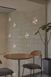 A well-lit dining area with two chairs and a wooden table, surrounded by potted plants and unique smiley face wall decor