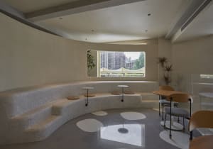 A well-lit room with a curved bench and chairs, three round tables, and a window, creating a comfortable and inviting atmosphere for socializing or dining
