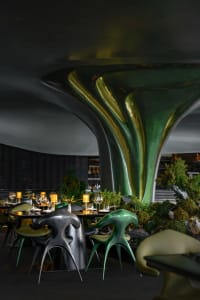 Modern dining space with chairs, wine glasses, and vases on marble and metal tables, warm and inviting ambiance with natural and artificial lighting