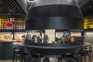 Industrial kitchen with a black countertop, stools, and dining chairs, featuring various kitchen items and a comfortable dining area