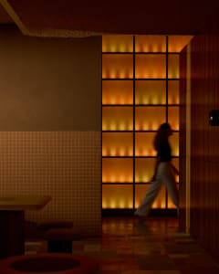 A woman walks down a hallway in an office building with a tiled floor, doors, and chairs for seating