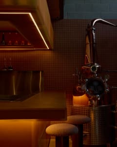 A vintage kitchen with orange tile walls, a sink, and various bottles on different surfaces, with a chair near the right side