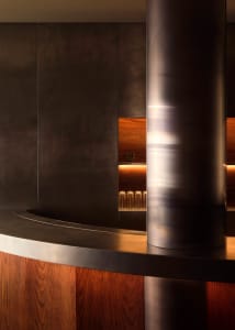A modern bar area with a metal pole supporting a countertop, surrounded by bottles and metallic design elements
