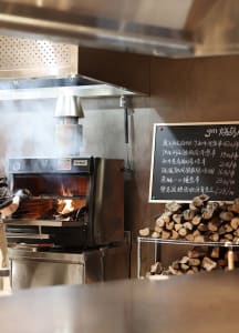 Industrial kitchen with a large oven and logs stacked against the wall, brick walls, and wooden accents